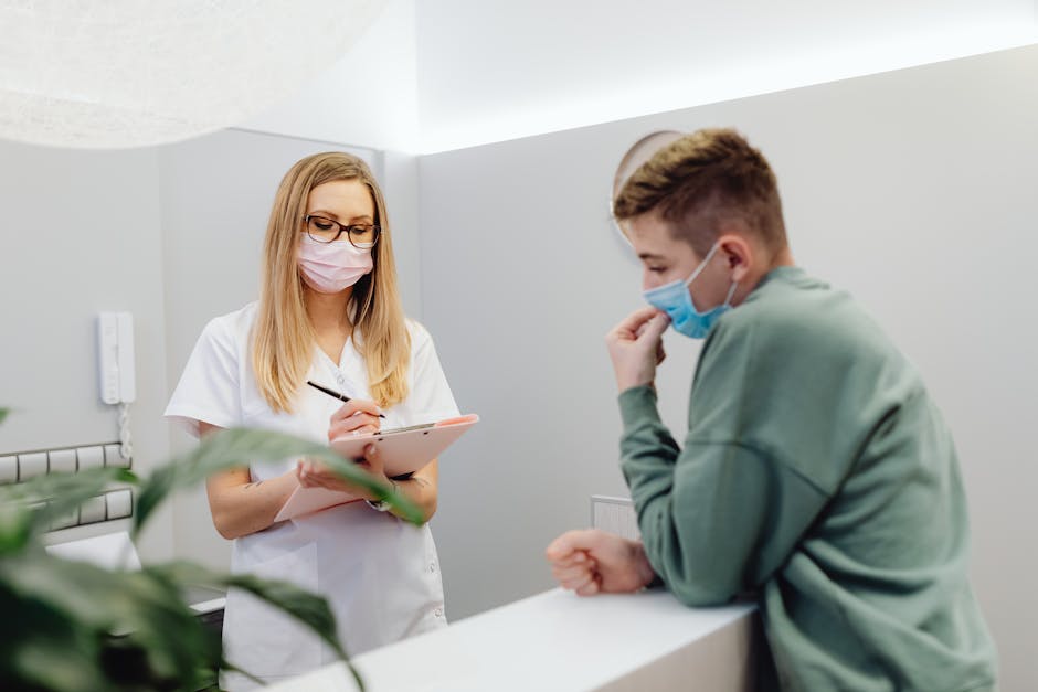 A healthcare worker consults a patient at a clinic reception, both wearing face masks.